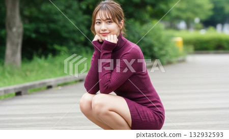 一位身穿酒紅色針織洋裝的女子蹲在公園裡微笑。 一位身穿酒紅色針織洋裝的女子蹲在公園裡微笑。 132932593