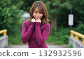 A woman in a knit dress smiles shyly with her hands on her collar 132932596