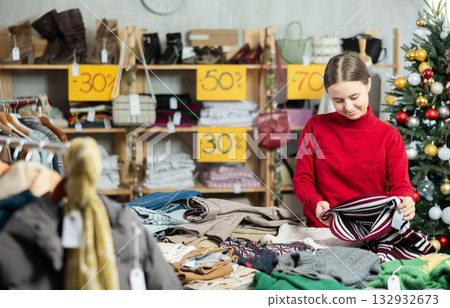 Teen girl picks up clothes and chooses sweater, New Year Eve sale 132932673