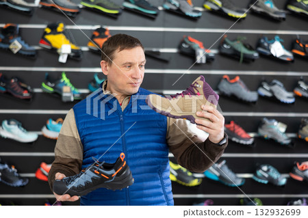 Attentive male athlete chooses sports winter shoes for hiking in sports store Attentive male athlete chooses sports winter shoes for hiking in sports store 132932699