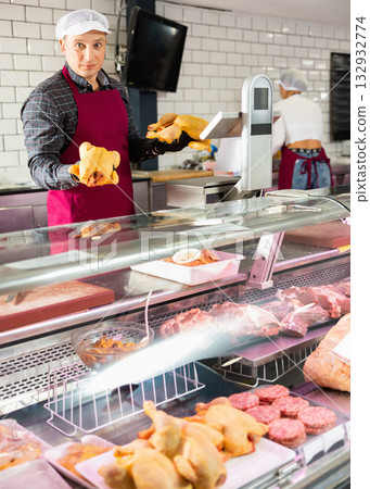 Butcher shop seller laying raw chickens in display case Butcher shop seller laying raw chickens in display case 132932774