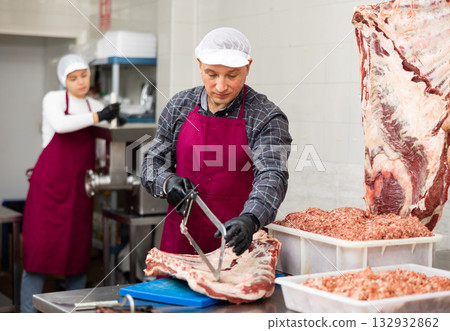 Happy female butcher sawing big chunk of beef meat in meat section of supermarket 132932862