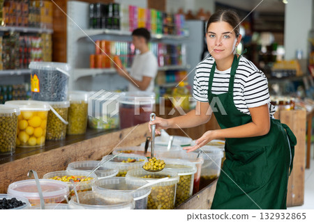 Seller girl in supermarket scooping marinated green olives 132932865