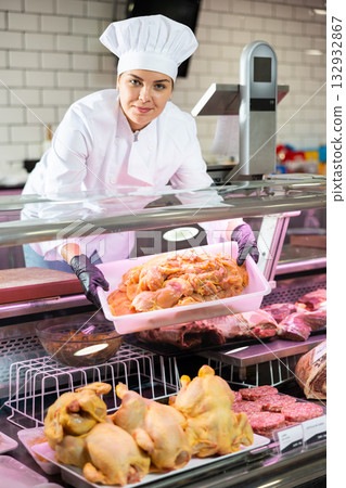 Smiling female butcher holding chicken fillet in butcher shop Smiling female butcher holding chicken fillet in butcher shop 132932867