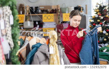 Teen girl is busy looking at clothes items in store, she choose jeans trousers 132932870