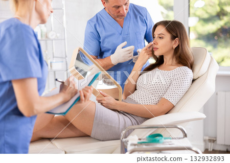 Man dermatologist examines skin of womans face, female nurse records data in client card 132932893