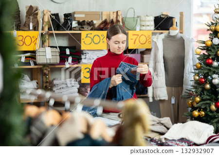 Teen girl is busy looking at clothes items in store, she choose jeans trousers 132932907