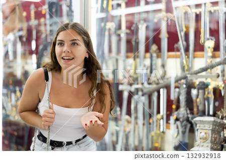 Female buyer holds in hands tests edged weapons in memorable gifts shop Female buyer holds in hands tests edged weapons in memorable gifts shop 132932918
