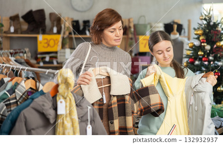 In sales area of store during Christmas sale, woman with teen daughter choose coat or jacket 132932937