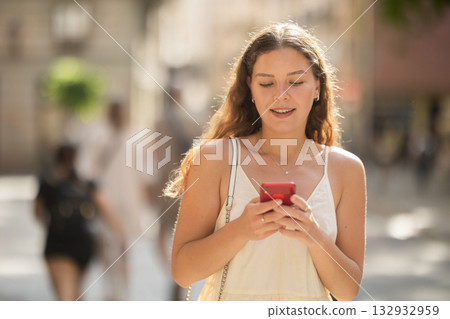 Young woman with phone walking along city street 132932959