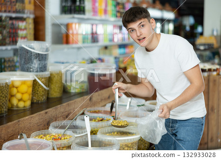Guy in supermarket scooping marinated green olives into plastic bag Guy in supermarket scooping marinated green olives into plastic bag 132933028