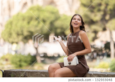 Cute young girl sitting on concrete fence in park during walk and relaxing in shade from daytime heat Cute young girl sitting on concrete fence in park during walk and relaxing in shade from daytime heat 132933048