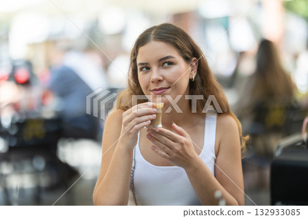 Smiling stylish young woman drinking espresso coffee sitting at cafe Smiling stylish young woman drinking espresso coffee sitting at cafe 132933085