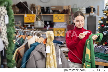 Teen girl picks up clothes and chooses sweater, New Year Eve sale 132933117
