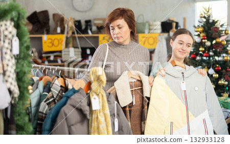 In sales area of store during Christmas sale, woman with teen daughter choose coat or jacket In sales area of store during Christmas sale, woman with teen daughter choose coat or jacket 132933128