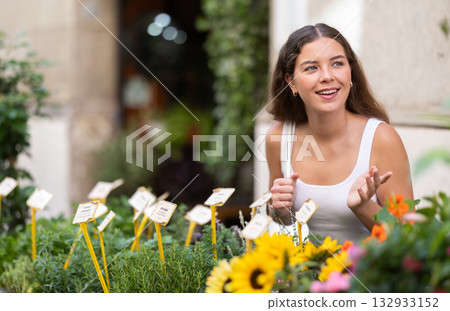 Cheerful young girl examining flowers on stalls of street market 132933152