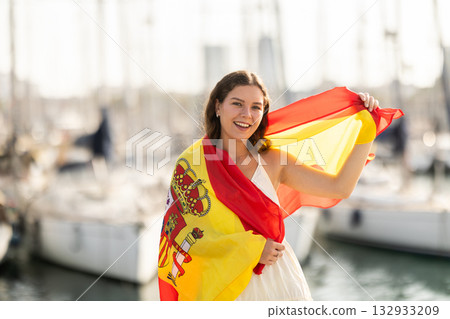 Woman waving national flag of Spain against seaport and yachts Woman waving national flag of Spain against seaport and yachts 132933209