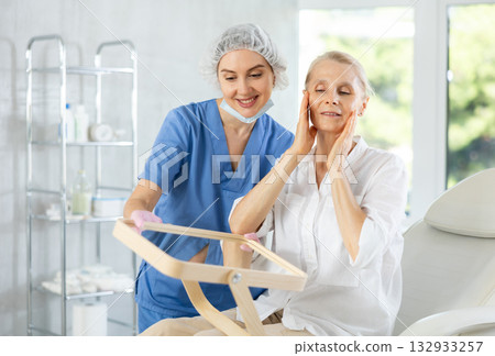 Satisfied old woman patient holding mirror sitting on clinical chair Satisfied old woman patient holding mirror sitting on clinical chair 132933257