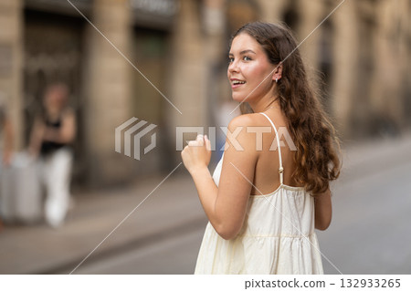 Cheerful girl in white dress walking along the street among architecture with bag Cheerful girl in white dress walking along the street among architecture with bag 132933265