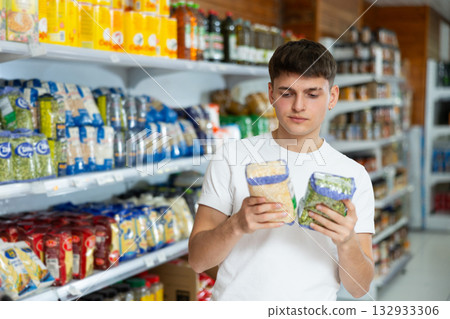 Guy carefully checks the information on product labels in hypermarket Guy carefully checks the information on product labels in hypermarket 132933306