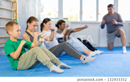 Group of people performing combat strikes sitting during group training 132933352
