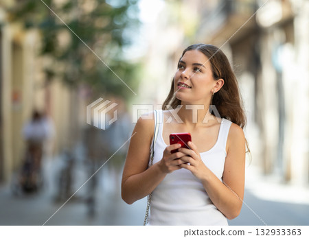 Young girl with mobile phone in her hands walking around the city and taking pictures of sights Young girl with mobile phone in her hands walking around the city and taking pictures of sights 132933363