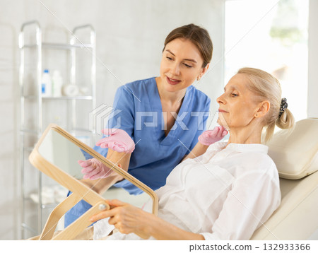 Female cosmetologist explaining facial procedure to elderly woman Female cosmetologist explaining facial procedure to elderly woman 132933366