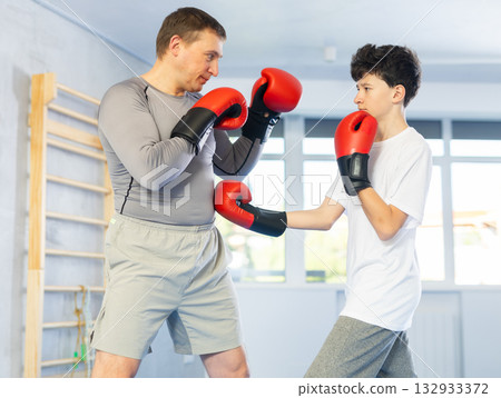 Middle-aged man and teenage boy training boxing during sports classes Middle-aged man and teenage boy training boxing during sports classes 132933372