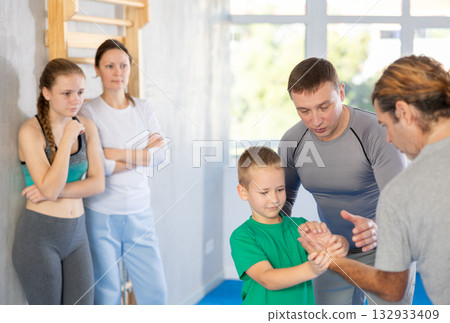 Trainer on man explains palm grab technique, boy, girl and woman watch and learn Trainer on man explains palm grab technique, boy, girl and woman watch and learn 132933409