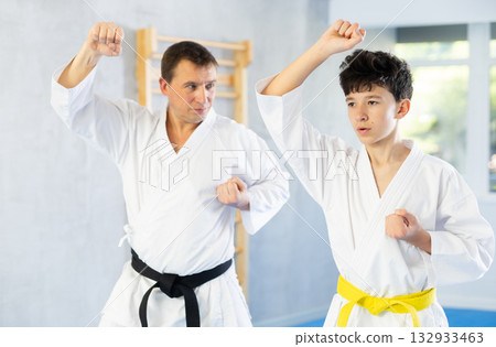 Karate trainer teaching block and punches to teenager in the gym Karate trainer teaching block and punches to teenager in the gym 132933463