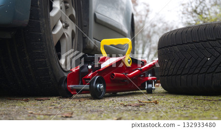 Red Hydraulic Floor Jack Under Car With Yellow Handle Beside Spare Tire On Ground Red Hydraulic Floor Jack Under Car With Yellow Handle Beside Spare Tire On Ground 132933480