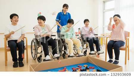 Several adults enjoying recreation in a bright indoor space. A user and support staff enjoying a fishing game during an indoor recreational activity. Several adults enjoying recreation in a bright indoor space. A user and support staff enjoying a fishing game during an indoor recreational activity. 132933609