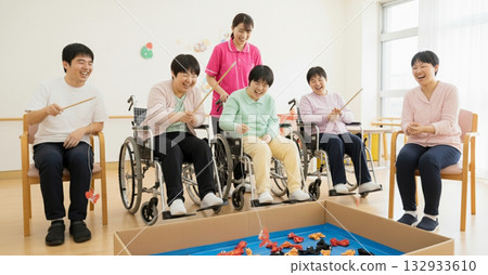 Several adults enjoying recreation in a bright indoor space. A user and support staff enjoying a fishing game during an indoor recreational activity. Several adults enjoying recreation in a bright indoor space. A user and support staff enjoying a fishing game during an indoor recreational activity. 132933610