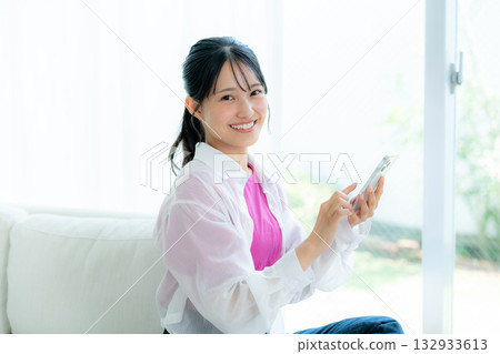 A young woman operating a smartphone in a room A young woman operating a smartphone in a room 132933613