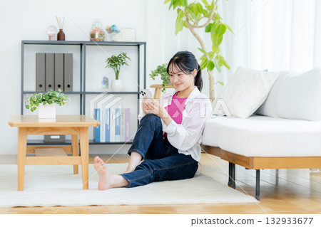 A young woman operating a smartphone in a room A young woman operating a smartphone in a room 132933677