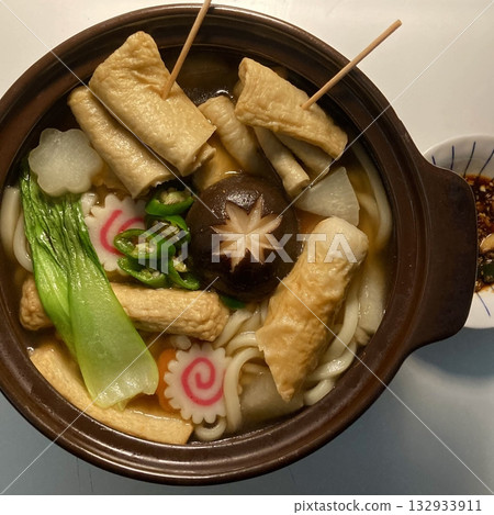 A warm bowl of udon noodles in a savory broth, topped with fresh scallions and tempura. This Japanese comfort food offers a perfect blend of chewy noodles and umami-rich flavors! 132933911