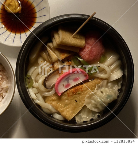 A bowl of udon noodles in a savory broth, topped with green onions, tempura, and a soft boiled egg. The thick, chewy noodles and rich flavors make it a comforting Japanese classic. A bowl of udon noodles in a savory broth, topped with green onions, tempura, and a soft boiled egg. The thick, chewy noodles and rich flavors make it a comforting Japanese classic. 132933954