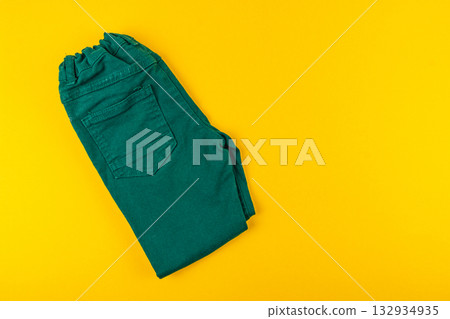 Colorful green pants folded neatly against a bright yellow background Colorful green pants folded neatly against a bright yellow background 132934935