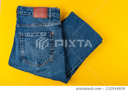 Jeans neatly folded on a bright yellow background in a simple layout 132934939