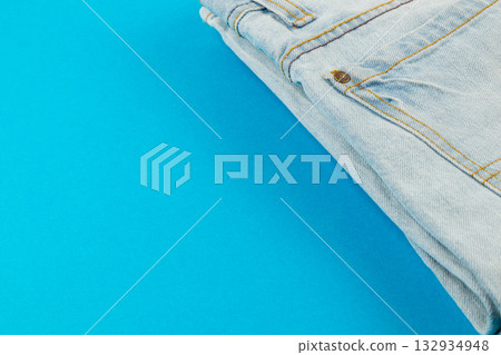 Stylish folded light blue jeans placed on a bright turquoise background Stylish folded light blue jeans placed on a bright turquoise background 132934948