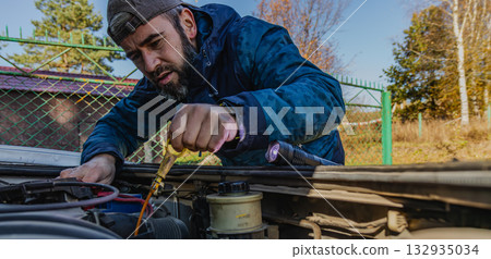 Man performs car maintenance in nature on a clear day Man performs car maintenance in nature on a clear day 132935034