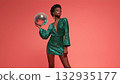 Model in green dress with disco ball, pink backdrop, created AI 132935177