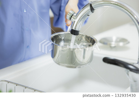 一位女士在廚房裡往鍋子裡倒水。 132935430