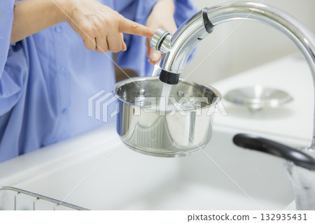 Woman pouring water into a pot in the kitchen Woman pouring water into a pot in the kitchen 132935431