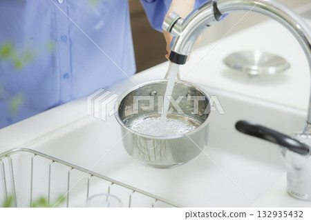 Woman pouring water into a pot in the kitchen Woman pouring water into a pot in the kitchen 132935432