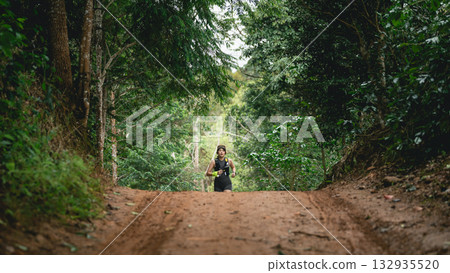 Person Running on a Dirt Path Through Lush Green Forest Surrounded by Trees and Natural Vegetation, Perfect for Outdoor Activity and Fitness Themes 132935520