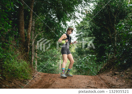 Energetic young woman jogging on a dirt trail in a lush green forest, showcasing fitness passion and love for nature during outdoor adventure Energetic young woman jogging on a dirt trail in a lush green forest, showcasing fitness passion and love for nature during outdoor adventure 132935521