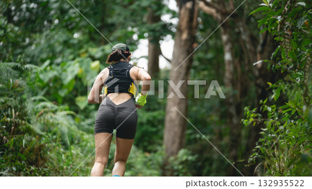 Female runner in sports gear jogging along a forest path surrounded by lush greenery, promoting health and fitness in an outdoor environment 132935522