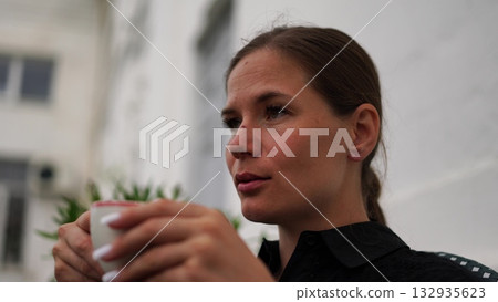 Woman Coffee Relaxation: Woman holds coffee cup outside, relaxing, during daylight, to enjoy beverage. 132935623