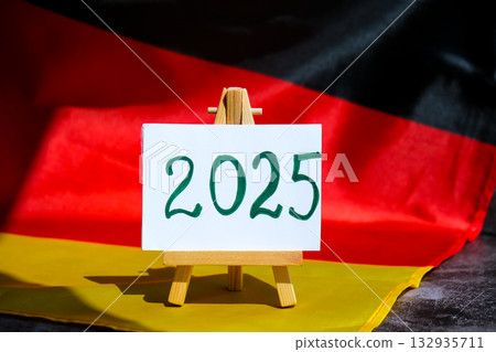 Paper note with text 2025 on National symbol of Germany. German wave silky flag background. Financial outlook planning, new year annual report Paper note with text 2025 on National symbol of Germany. German wave silky flag background. Financial outlook planning, new year annual report 132935711